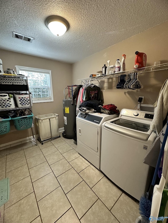 washroom featuring water heater, light tile patterned floors, a textured ceiling, and washer and clothes dryer