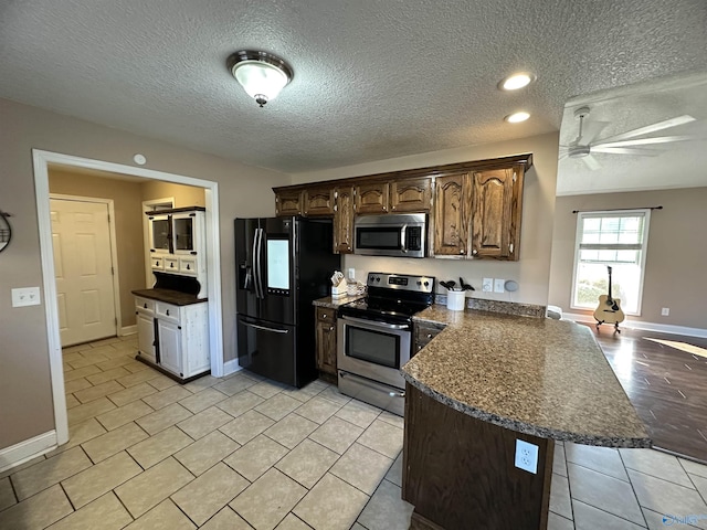 kitchen featuring light tile patterned floors, kitchen peninsula, ceiling fan, appliances with stainless steel finishes, and a textured ceiling