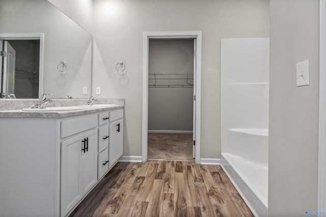 full bathroom with a sink, wood finished floors, double vanity, baseboards, and a spacious closet