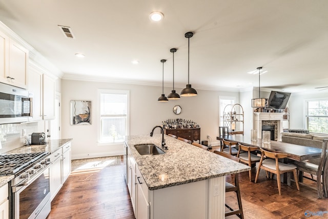 kitchen featuring stainless steel appliances, sink, decorative light fixtures, white cabinets, and an island with sink