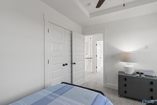 bedroom featuring ceiling fan, a closet, a tray ceiling, and light carpet