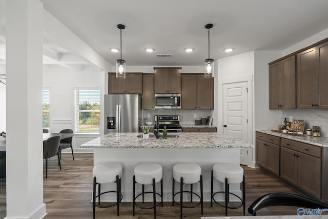 kitchen with stainless steel appliances, light stone countertops, and a center island with sink