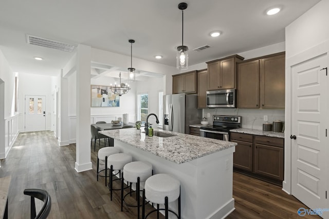 kitchen featuring appliances with stainless steel finishes, decorative light fixtures, sink, light stone counters, and a center island with sink