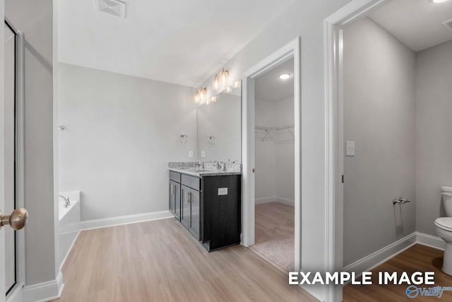 bathroom with hardwood / wood-style flooring, vanity, toilet, and a bath