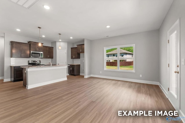 kitchen featuring hanging light fixtures, an island with sink, stainless steel appliances, and light hardwood / wood-style flooring