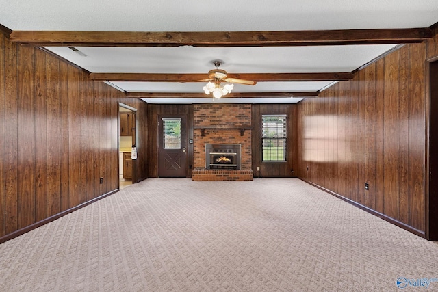 708 Apache St NW, Hartselle, AL 35640 - unfurnished living room featuring wooden walls, a ceiling fan, beam ceiling, a fireplace, and light colored carpet