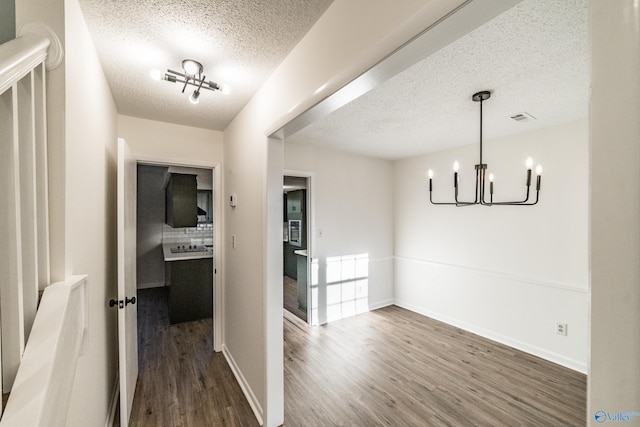 unfurnished dining area with dark wood-type flooring, a textured ceiling, and an inviting chandelier