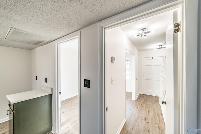 corridor featuring light wood-type flooring and a textured ceiling