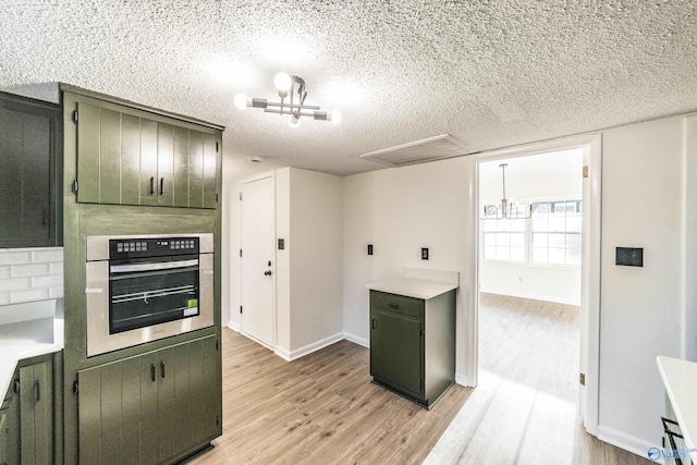 kitchen with stainless steel oven, green cabinets, a textured ceiling, a notable chandelier, and light hardwood / wood-style floors