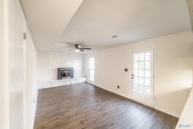 unfurnished living room with a textured ceiling, a wood stove, plenty of natural light, and dark hardwood / wood-style floors