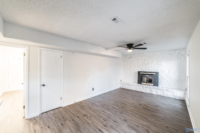 unfurnished living room with hardwood / wood-style flooring, ceiling fan, a wood stove, and a textured ceiling