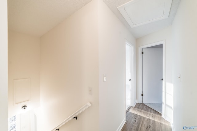 corridor featuring a textured ceiling, light hardwood / wood-style flooring, and lofted ceiling