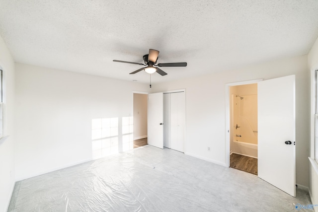 unfurnished bedroom featuring a textured ceiling, light colored carpet, ensuite bath, and ceiling fan