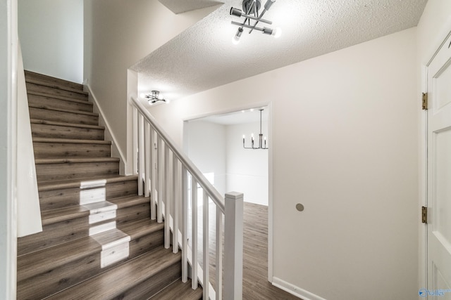 stairway with hardwood / wood-style floors, a textured ceiling, and an inviting chandelier