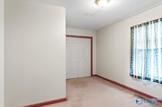 unfurnished bedroom featuring light carpet, a textured ceiling, and a closet