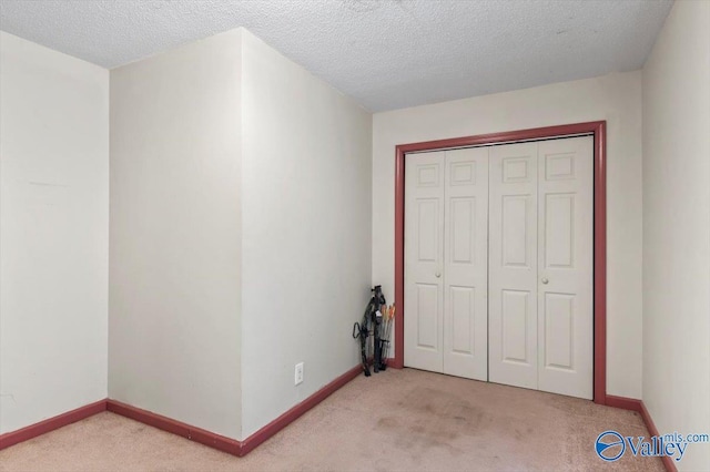 unfurnished bedroom featuring light colored carpet, a textured ceiling, and a closet