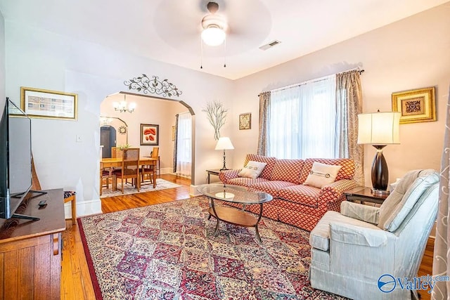 living room with wood finished floors, baseboards, visible vents, arched walkways, and ceiling fan