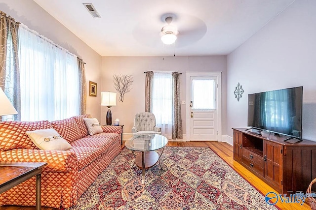 living area with visible vents, baseboards, light wood-style flooring, and a ceiling fan