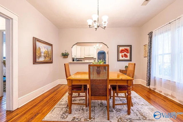 dining area with baseboards, wood finished floors, visible vents, and a chandelier