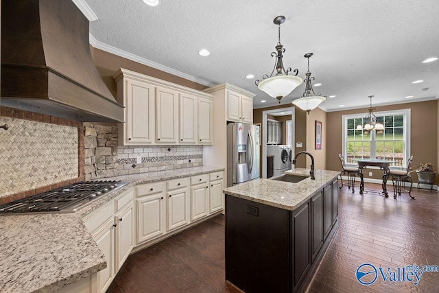 kitchen featuring premium range hood, hanging light fixtures, stainless steel appliances, light stone counters, and a center island with sink