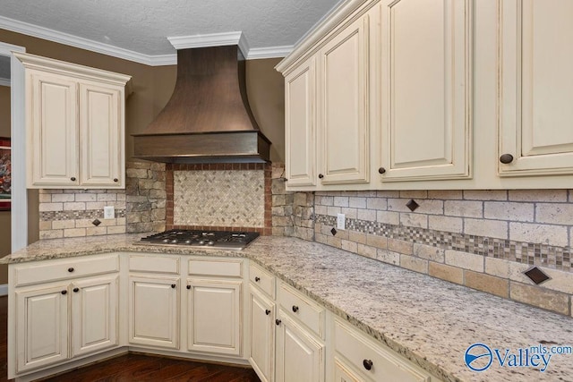 kitchen with cream cabinetry, custom exhaust hood, light stone countertops, and stainless steel gas cooktop