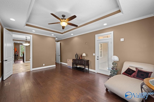 living area with a tray ceiling, dark wood-type flooring, and ceiling fan