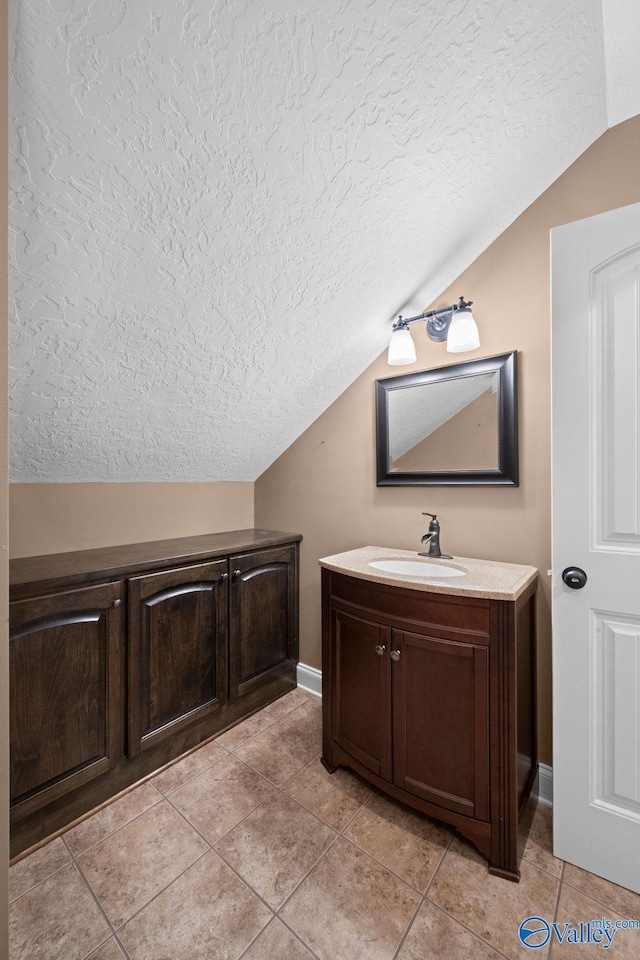 bathroom featuring tile patterned floors, vanity, vaulted ceiling, and a textured ceiling