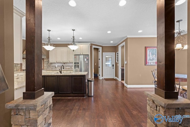 kitchen with sink, dark wood-type flooring, stainless steel fridge, hanging light fixtures, and light stone counters