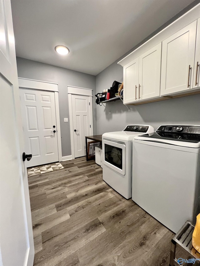 laundry room featuring cabinet space, washer and dryer, baseboards, and wood finished floors