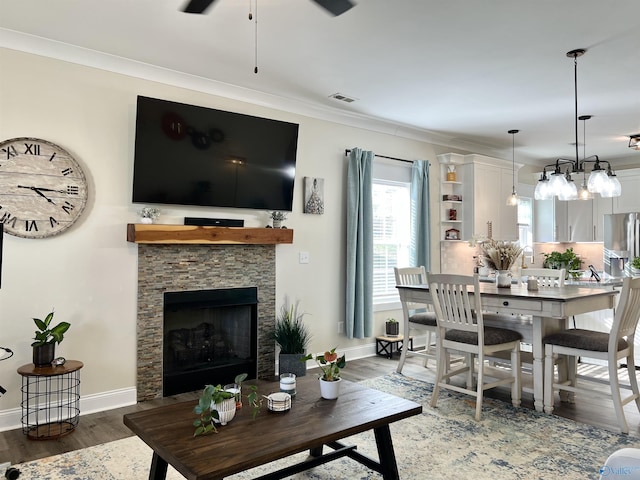 living area featuring visible vents, wood finished floors, a stone fireplace, crown molding, and baseboards