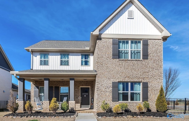 view of front of property featuring a porch, brick siding, a shingled roof, fence, and board and batten siding