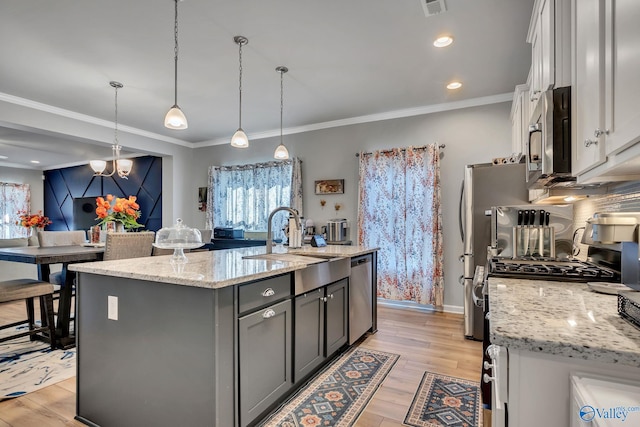 kitchen featuring a kitchen island with sink, stainless steel appliances, a sink, light wood-style floors, and decorative backsplash