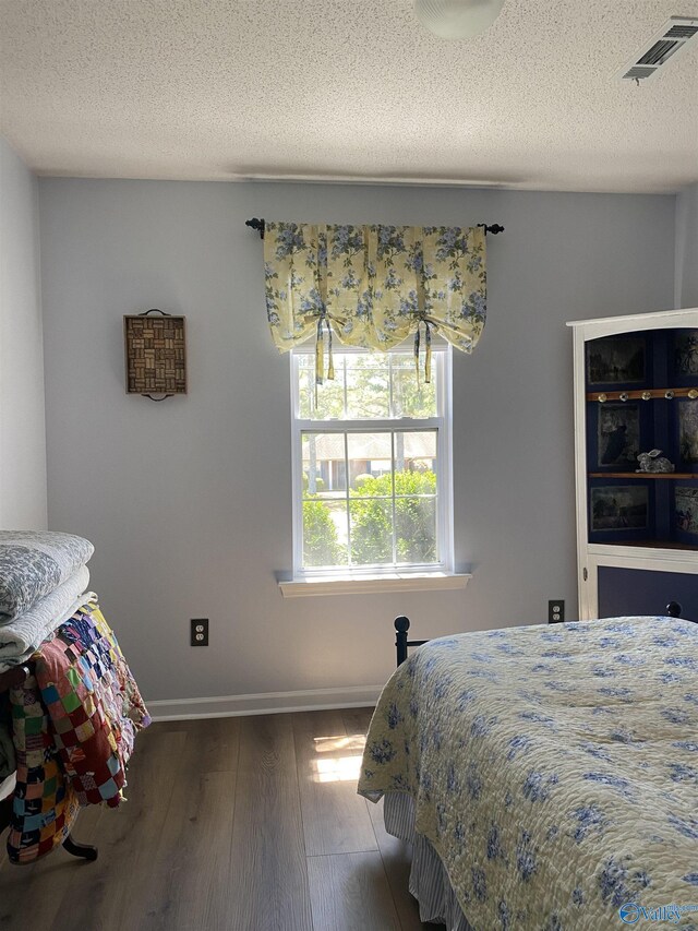 bedroom with a textured ceiling, wood finished floors, baseboards, and visible vents