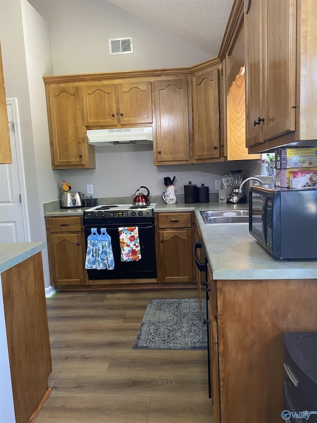 kitchen with vaulted ceiling, under cabinet range hood, visible vents, black appliances, and wood finished floors