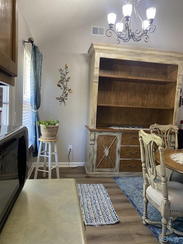 dining area with visible vents, wood finished floors, a chandelier, and vaulted ceiling