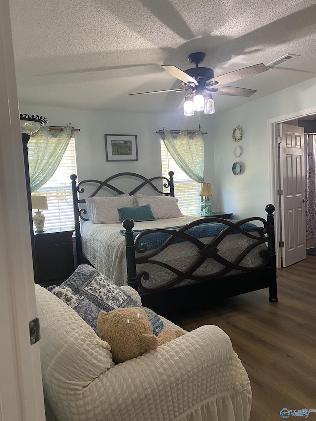 bedroom with a textured ceiling, wood finished floors, ceiling fan, and visible vents