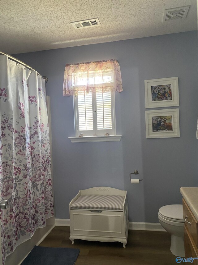 bathroom with toilet, a textured ceiling, wood finished floors, and visible vents