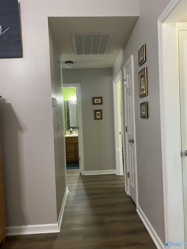 hallway with a sink, visible vents, baseboards, and dark wood finished floors