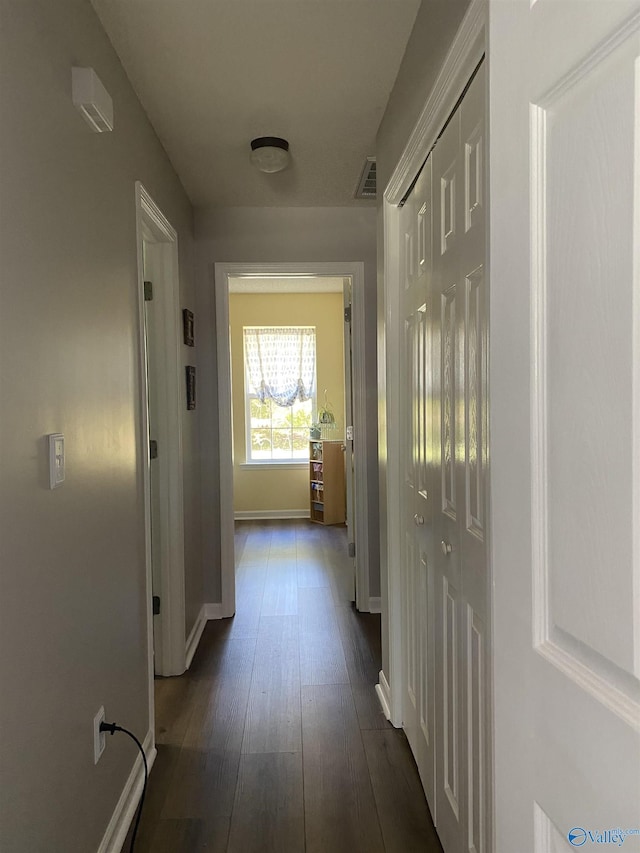 hall with visible vents, baseboards, and dark wood-style floors