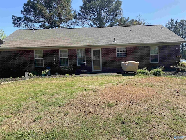 rear view of property with roof with shingles, brick siding, and a lawn