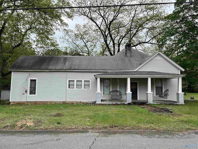 view of front of property featuring a porch, a front yard, metal roof, and a chimney