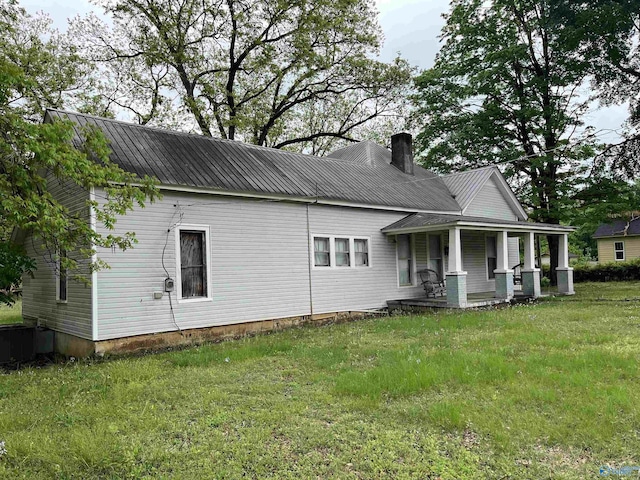 back of house with a porch, a lawn, metal roof, and a chimney