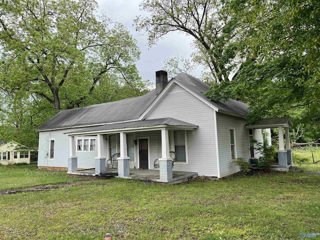 view of front facade with a chimney, a porch, and a front lawn