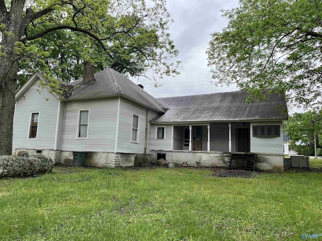 rear view of house with covered porch, a chimney, metal roof, and a lawn