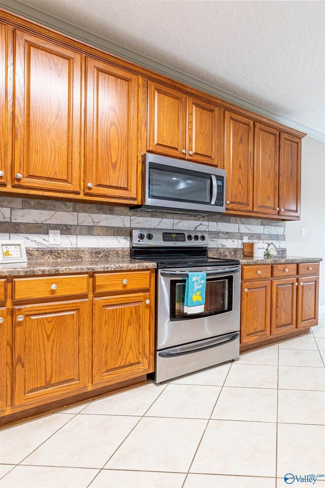 2115 James Dr, Southside, AL 35907 - kitchen with stainless steel appliances, brown cabinets, backsplash, light tile patterned floors, and a textured ceiling