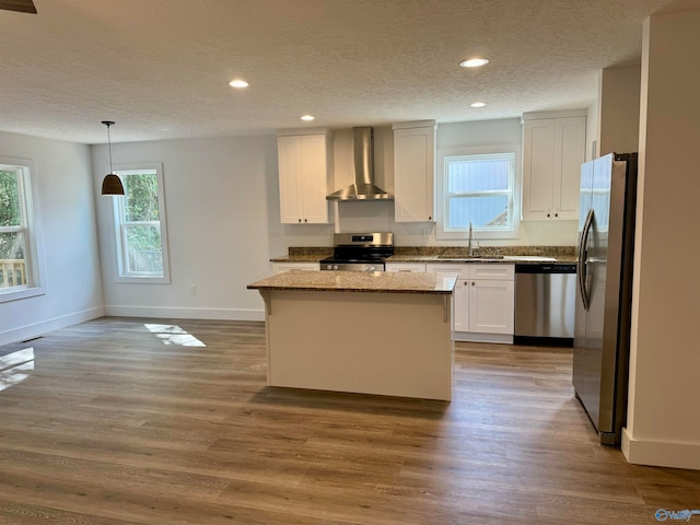 kitchen featuring sink, hanging light fixtures, a kitchen island, wall chimney range hood, and appliances with stainless steel finishes