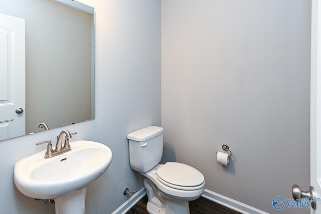 half bath featuring toilet, baseboards, a sink, and wood finished floors