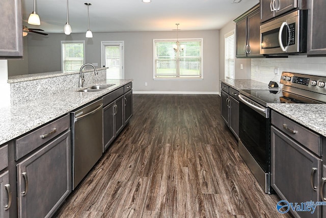 kitchen with light stone countertops, baseboards, a sink, dark wood finished floors, and appliances with stainless steel finishes