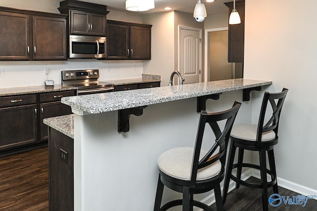 kitchen with dark brown cabinets, baseboards, a breakfast bar area, dark wood finished floors, and appliances with stainless steel finishes