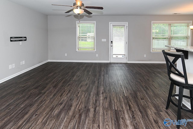 unfurnished living room with dark wood-style flooring, a ceiling fan, baseboards, and a healthy amount of sunlight